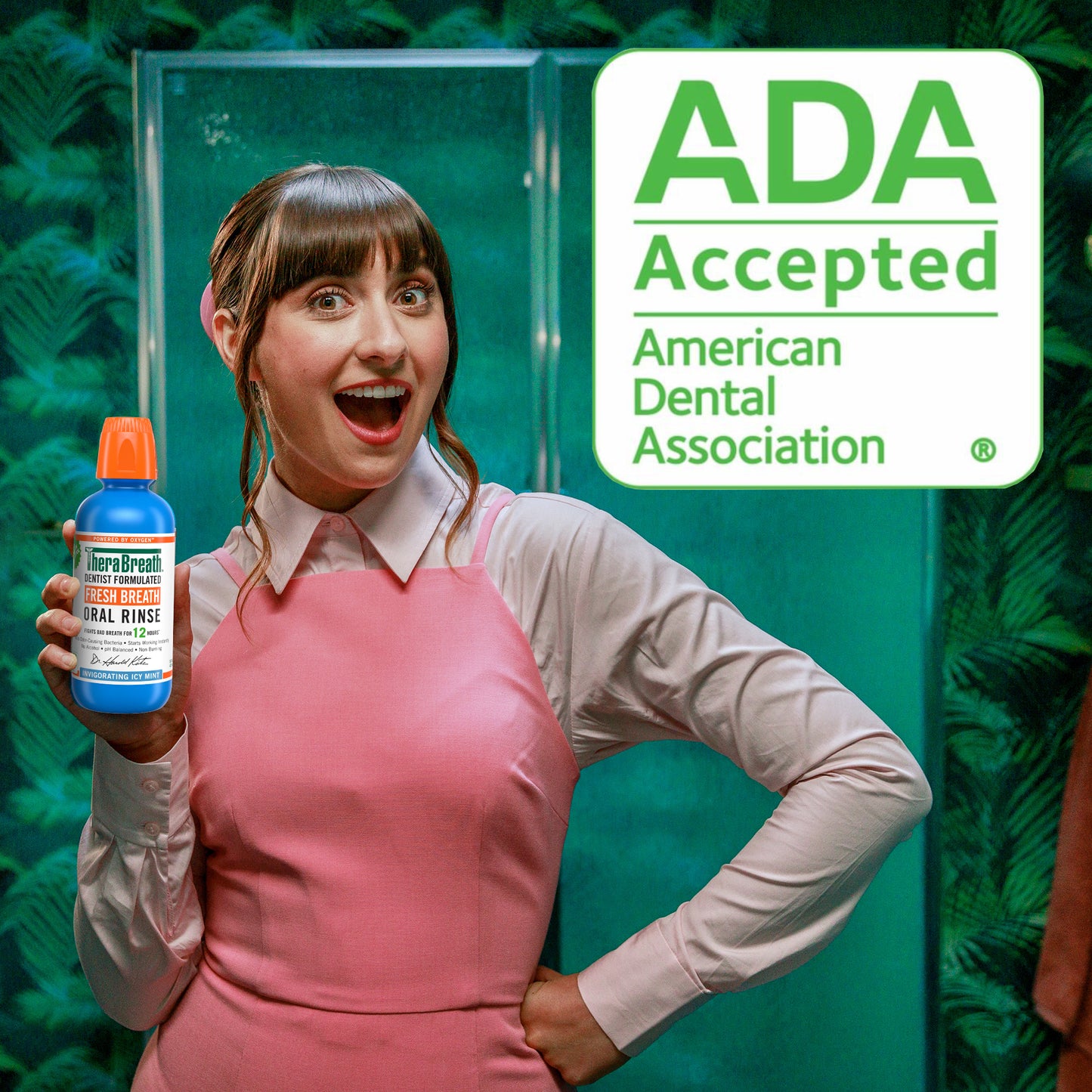 Woman smiling holding a bottle of TheraBreath Fresh Breath Oral Rinse Invigorating Icy Mint - a sign says "ADA Accepted" showing that it is accepted by the American Dental Association