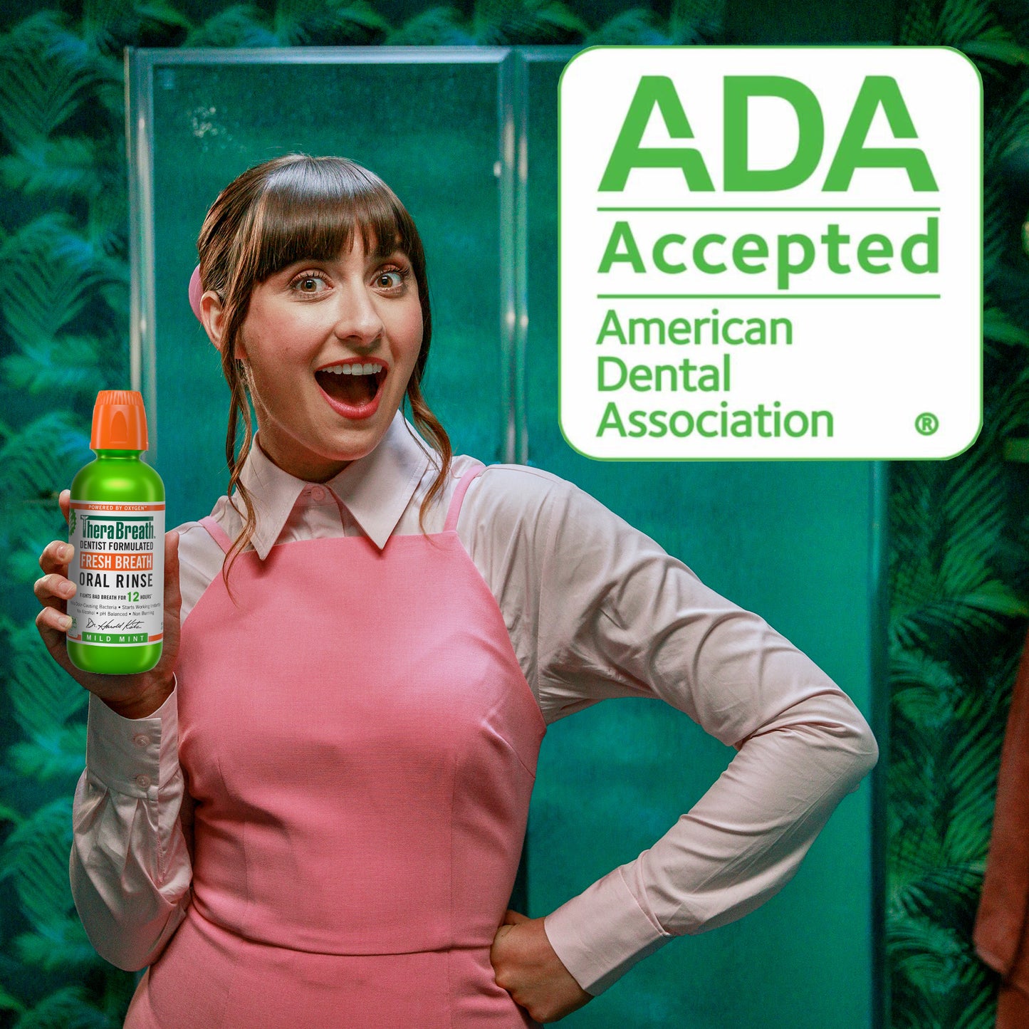 Woman smiling holding a bottle of TheraBreath Fresh Breath Oral Rinse Mild Mint - a sign says "ADA Accepted" showing that it is accepted by the American Dental Association