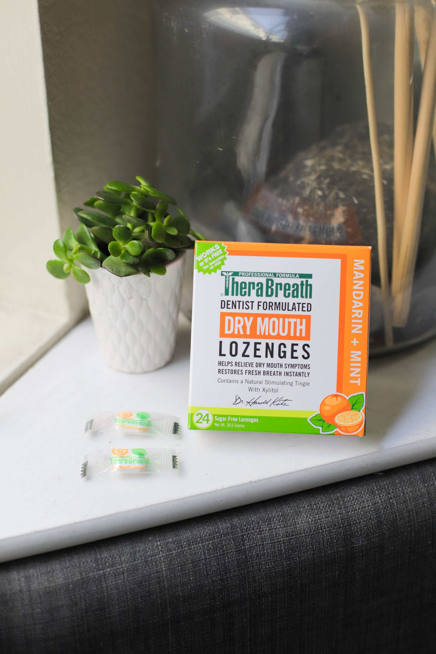 A box of TheraBreath Dry Mouth Lozenges in Mandarin Mint sits on the counter with a small plant