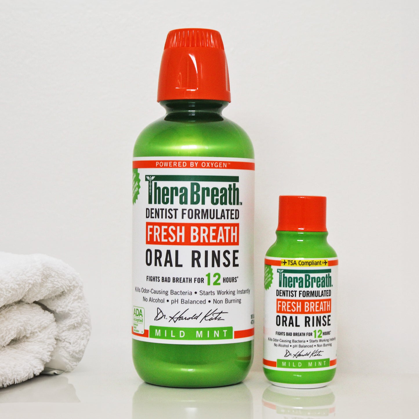 Two bright green bottles of TheraBreath Fresh Breath Oral Rinse in Mild Mint sit side by side on a bathroom counter. One normal sized, the other is a small travel size bottle.