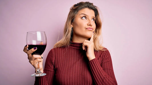 Woman holding a glass of red wine while thinking, illustrating questions about alcohol and canker sores
