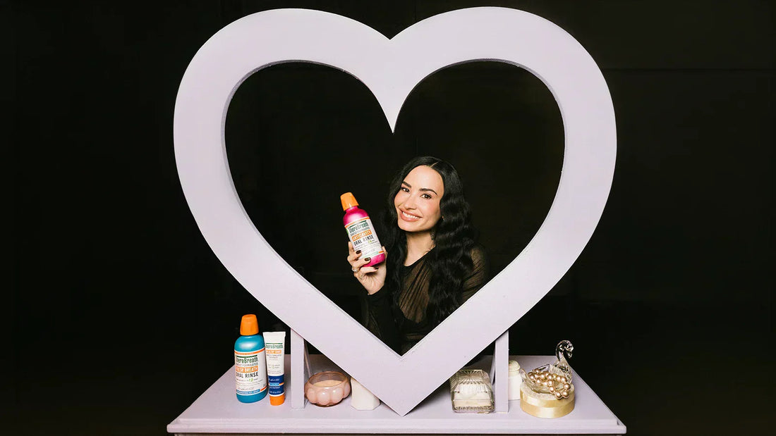 Demi Lovato smiling and holding TheraBreath Anticavity Oral Rinse, framed by a white heart-shaped display
