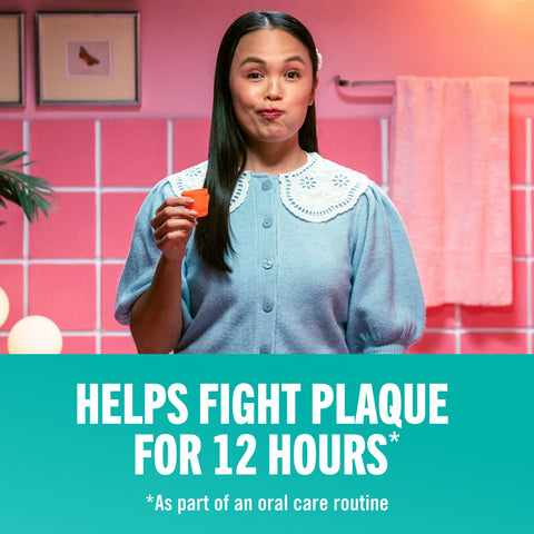 A woman holding an orange bottle cap while rinsing her mouth with therabreath oral rinse that helps fight plaque for 12 hours.