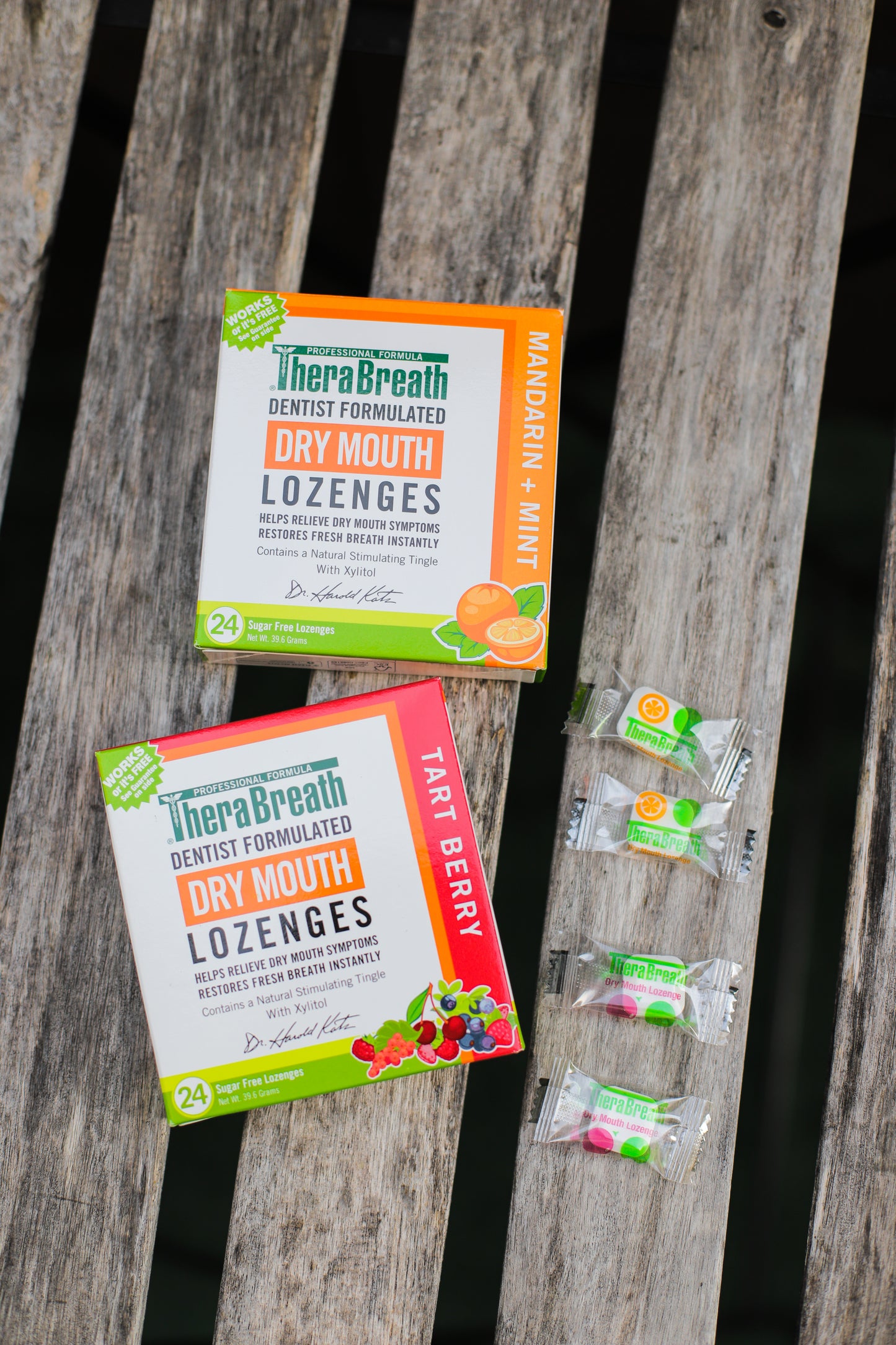 Boxes of TheraBreath Dry Mouth Lozenges in Tart Berry and Mandarin Mint sit on wooden slats.